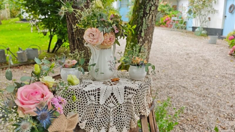 Composition florale romantique avec dentelle, fleurs fraîches et objets anciens dans une cour arborée